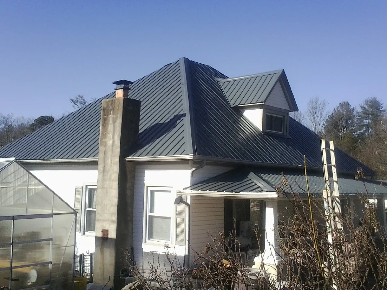 Dark blue standing seam metal roof on a white farmhouse with dormer — Slate & Tile Roof Repair by Roofing Brothers in Emden