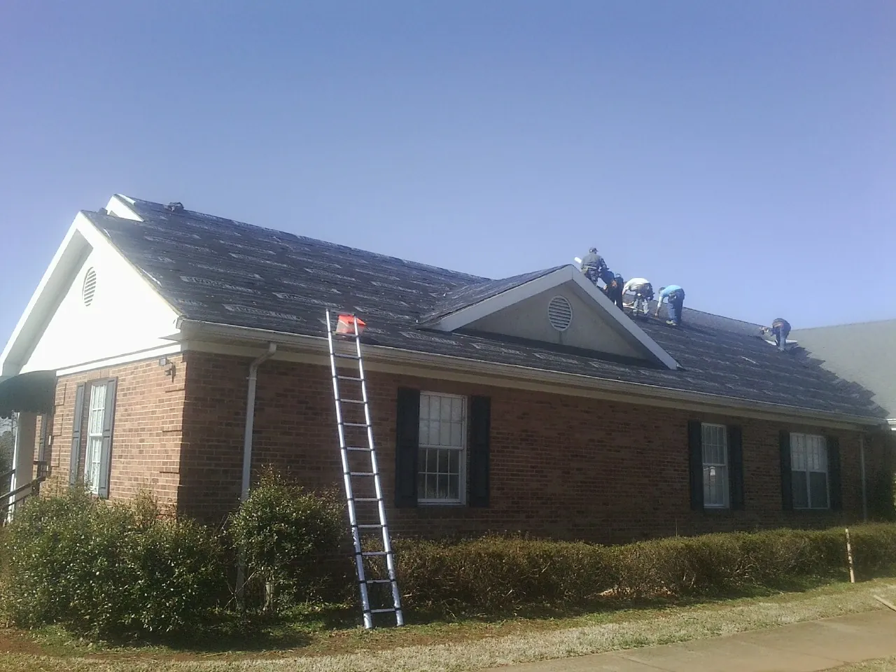 Crew tearing shingles off a brick ranch roof with a ladder set — Emergency Roof Repair work by our crew in Emden
