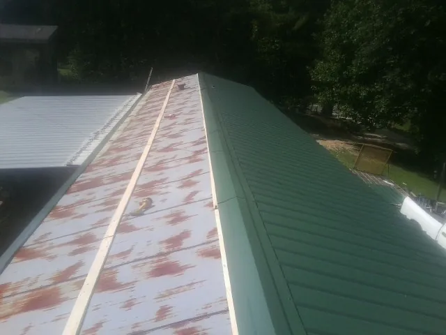 Old rusted panels beside newly installed green metal roofing — Wind Damage Roof Repair by Roofing Brothers in Emden